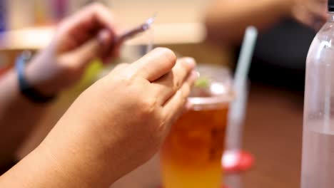 a person unwraps a straw and prepares to drink iced tea at a casual indoor table, with warm lighting and shallow depth of field