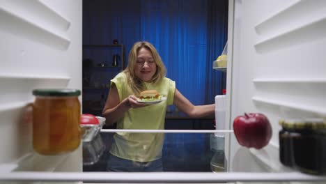 woman eating late-night snack from refrigerator