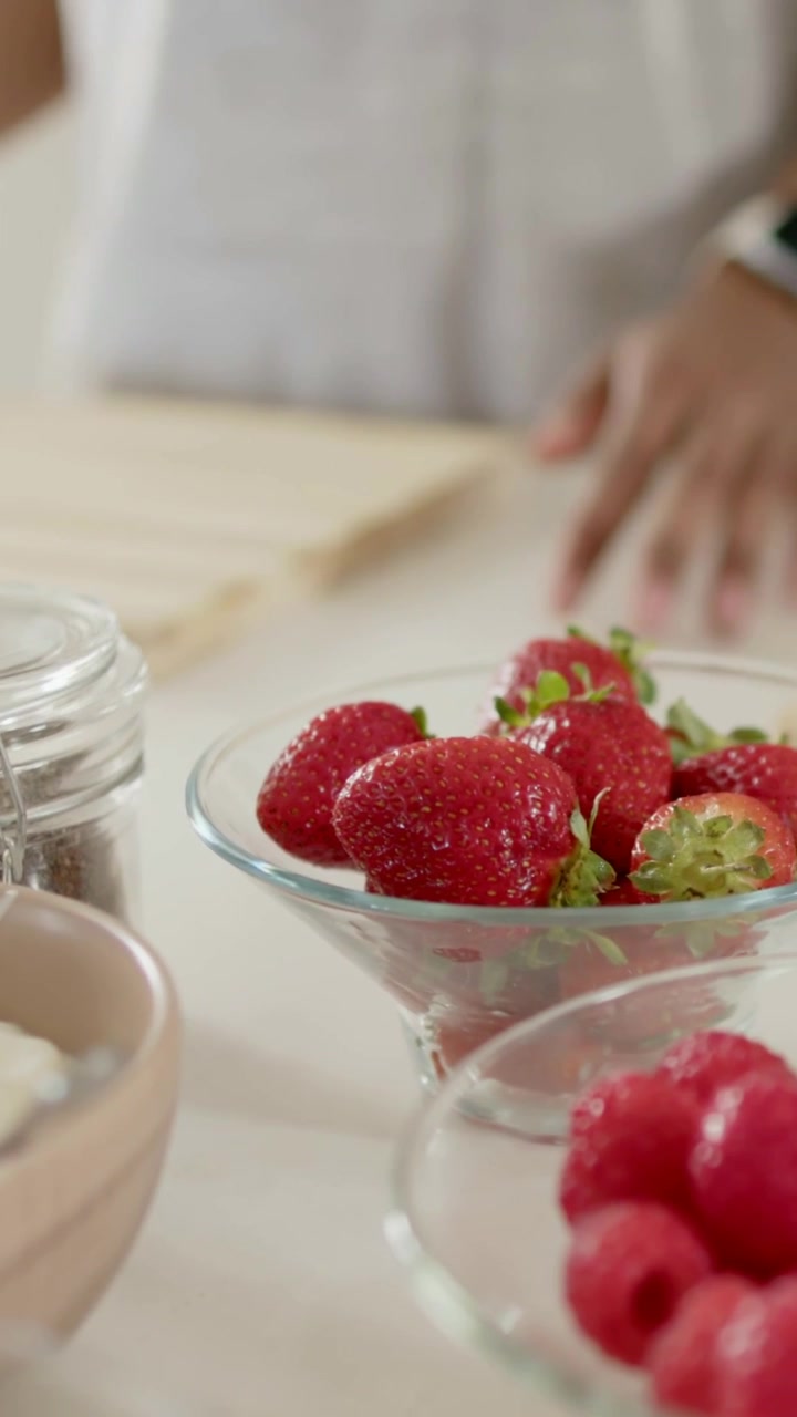 Vertical video: Hand reaching woman in tank grabbing banana in kitchen making snack with raspberry