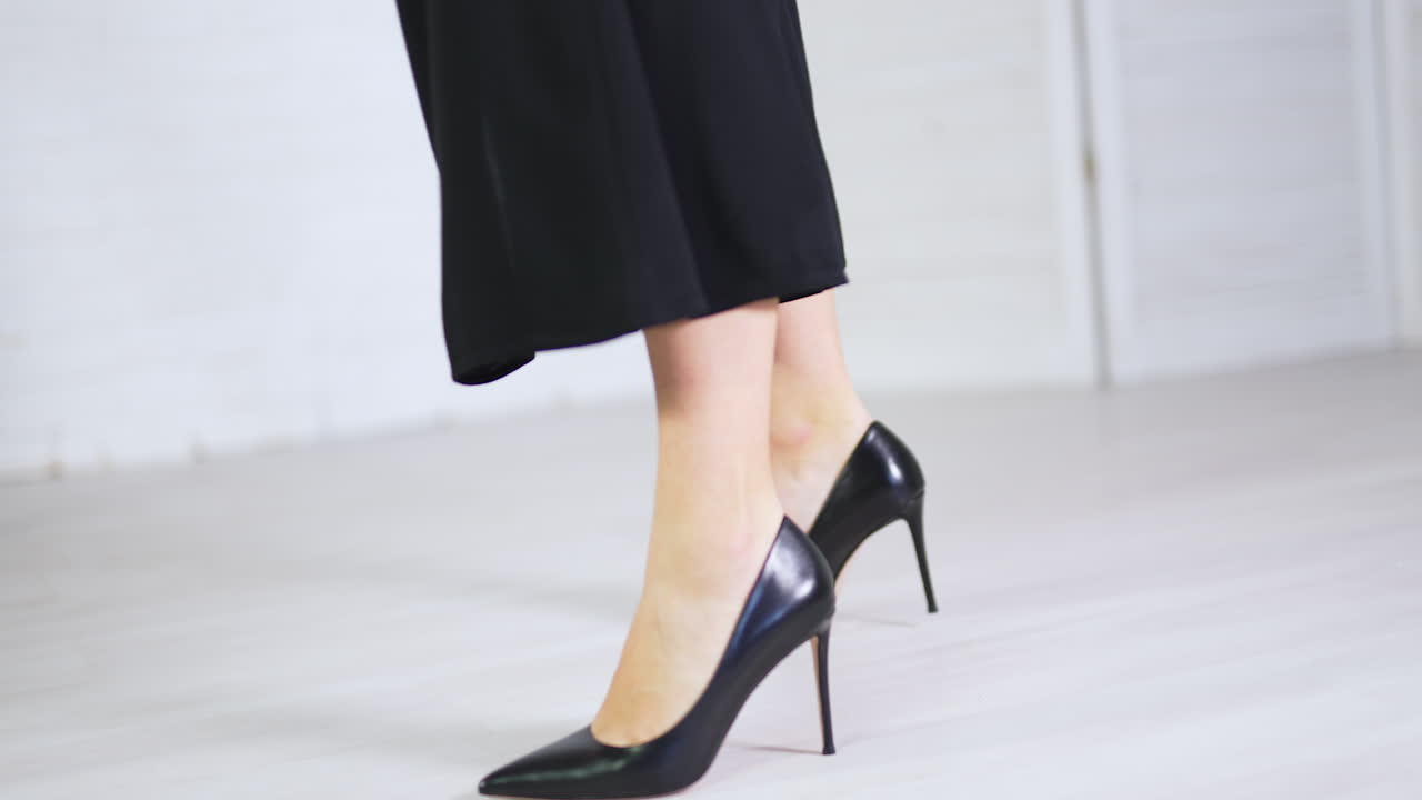 Elegant classic black shoes demonstration. Woman in long black skirt showing the high-heeled stiletto footwear. White backdrop.