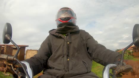 A-action-shot-of-an-African-man-wearing-a-helmet-while-steering-a-motor-bikes-handle-bars-rides-through-a-African-slum