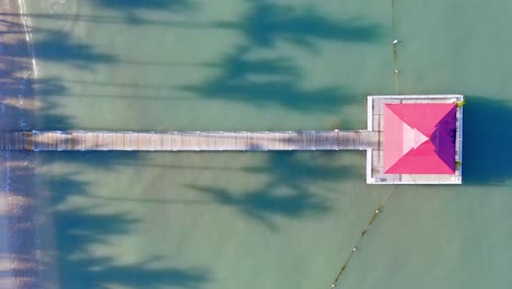 Jetty-with-gazebo-in-ocean,-exotic-beachfront-with-palms