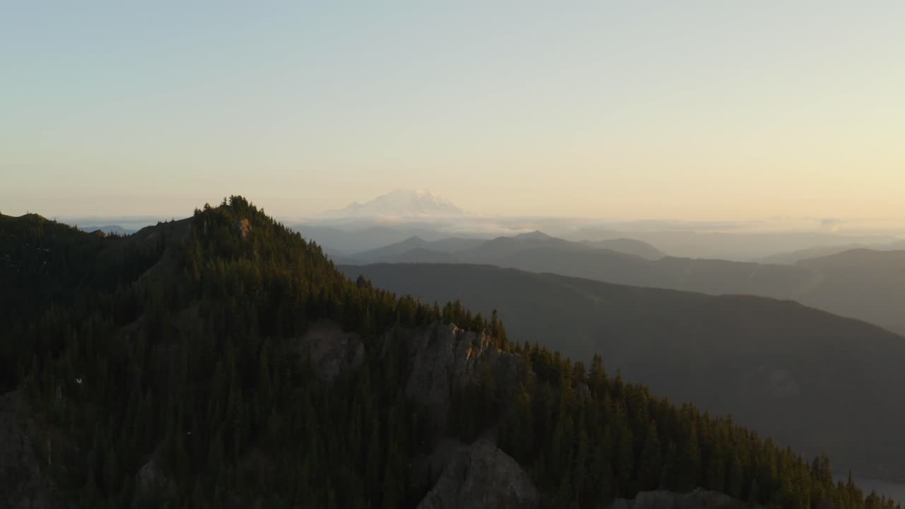 Slow moving parallax effect with ridge in foreground and mountain range in background, aerial shot during dusk, golden hour