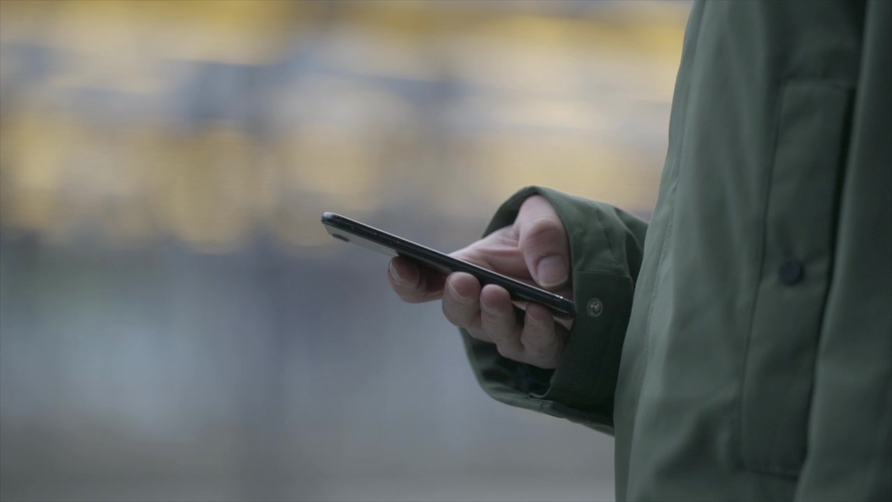 Nærbillede af hænder, der scroller på en smartphone. Togstation