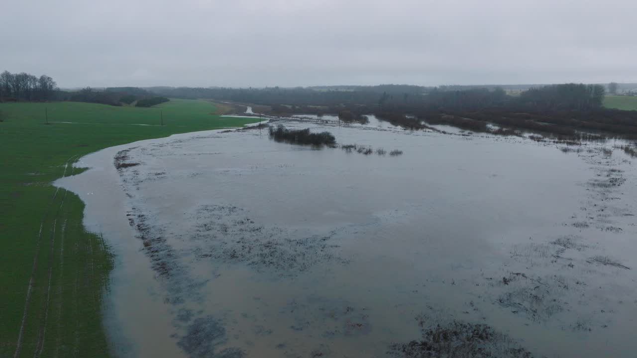 Aerial establishing view of high water in springtime, Alande river flood, brown and muddy water, agricultural fields under the water, overcast day, wide drone shot moving forward