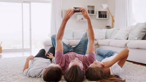 Padre-E-Hijos-Tumbados-En-Una-Alfombra-Y-Posando-Para-Un-Selfie-En-Casa