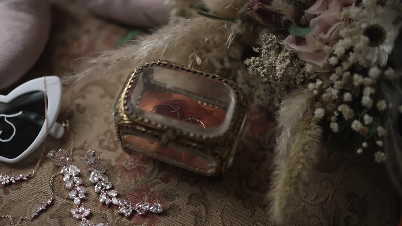 Close up of bridal jewelry flowers and glass box arranged on patterned chair