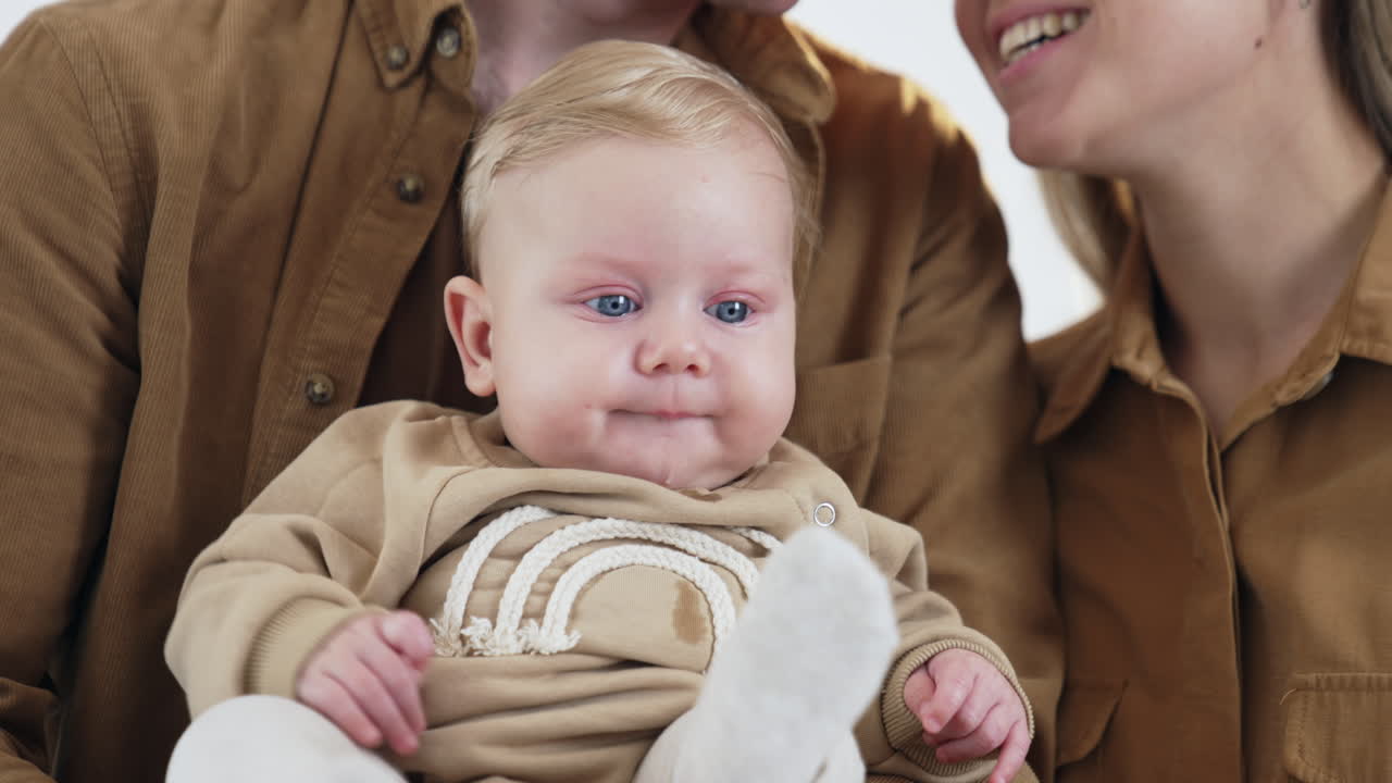 Adorable baby boy with blond hair and bog blue eyes. Little infant kid sitting comfortably in dad's hands. Close up.