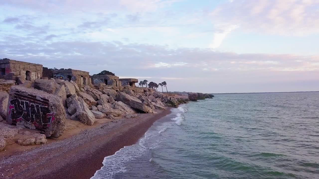 вид с воздуха на заброшенные приморские фортификационные сооружения в северных фортах кароста на берегу балтийского моря в лиепае, латвия, спокойное море вечером, съемка с широкоугольного дрона с низкой высоты, движущегося вперед