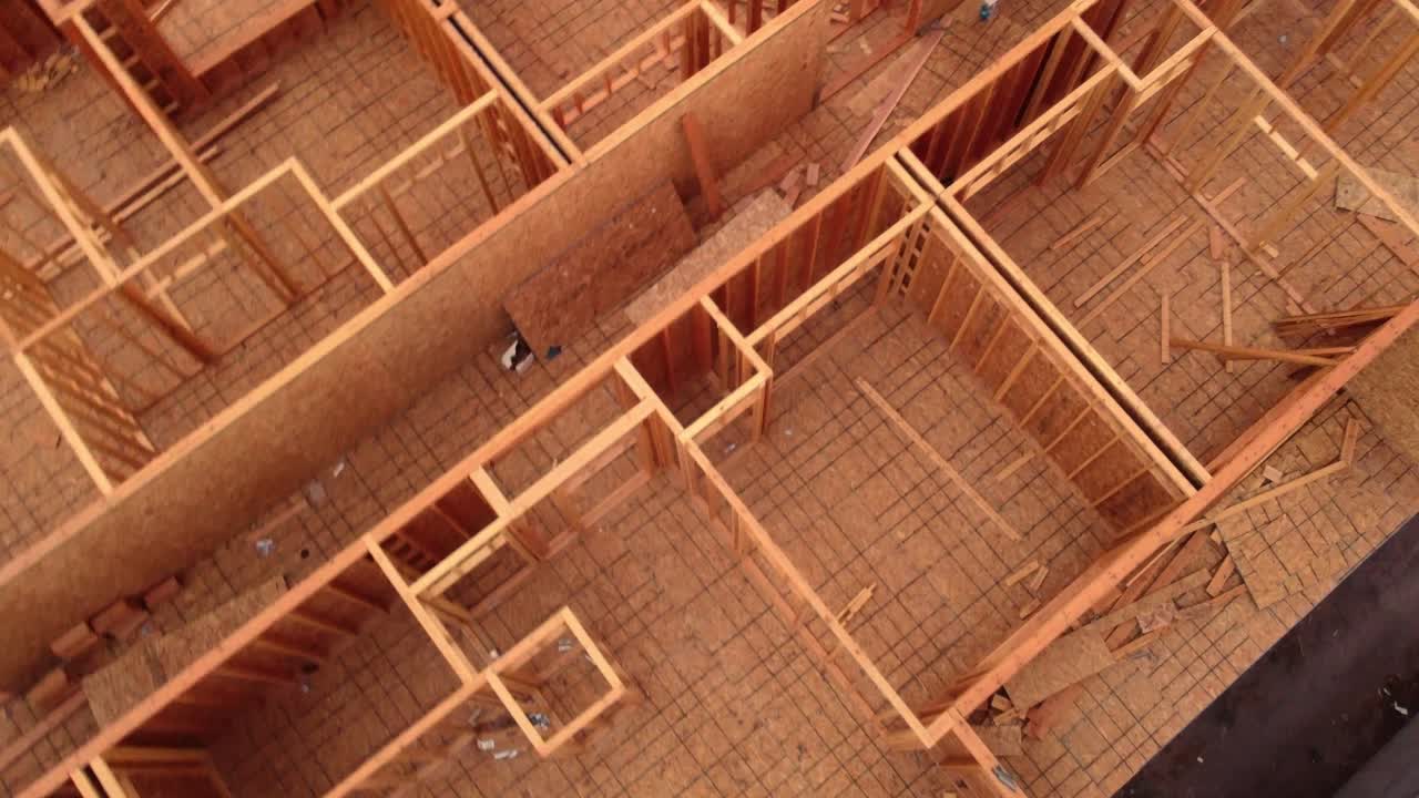 Wood framed construction site left abandoned shut down as work stopped due to pandemic supply chain shutdown as drone flys up over and behind a 4 story apartment condo building