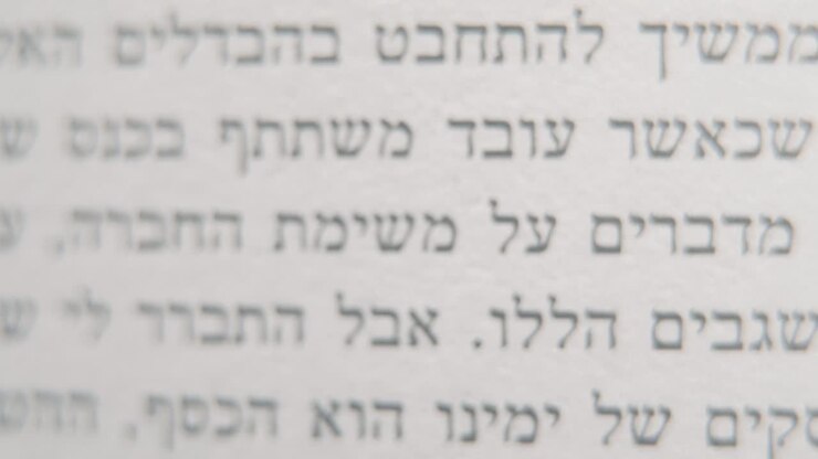 A macro smooth and detailed tilt down shot of a book in Hebrew, black letters on white paper, 4K video