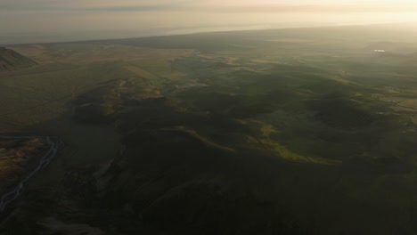 tomada de un avión no tripulado de un vasto paisaje islandés al anochecer, con colinas onduladas, llanuras distantes y luz suave y desvanecida a través del terreno