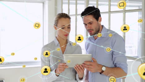 Animation-of-network-of-people-and-chat-icons-over-caucasian-male-and-female-colleague-using-tablet