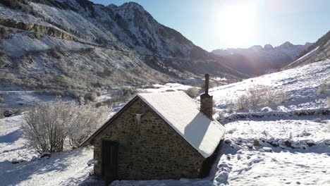 aerial shot of a lonely snowy rustic house in the middle of the mountains of a valley in the spanish pyrenees in a sunny day with the door open