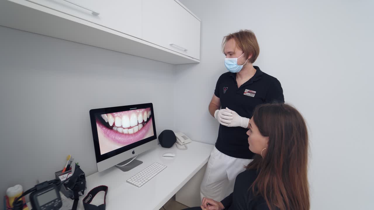 Stomatologist giving consultation to a woman. Doctor shows young patient the situation of her teeth. Dentist shows photo of woman's teeth on the screen in dental office.