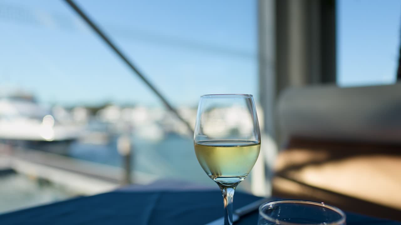 Water is poured from a jug into a wine glass on a sunlit marina table