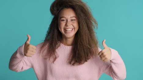 mujer caucásica de cabello rizado con los pulgares hacia arriba delante de la cámara.