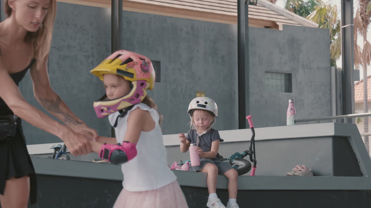 madre enseñando a su hija a patinar mientras el niño pequeño descansa