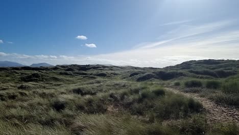 Slow-motion-panning-across-grassy-sand-dunes-landscape-with-misty-Snowdonia-mountain-range-on-sunrise-horizon