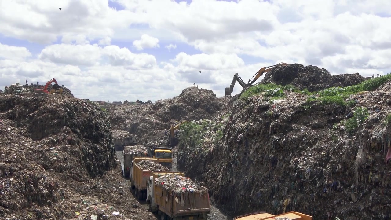 A massive mountain of rubbish at Dandora dumpsite as shovels and heavy trucks unload incoming waste. Exposes the industrial scale of East Africa's urban garbage crisis and land pollution.