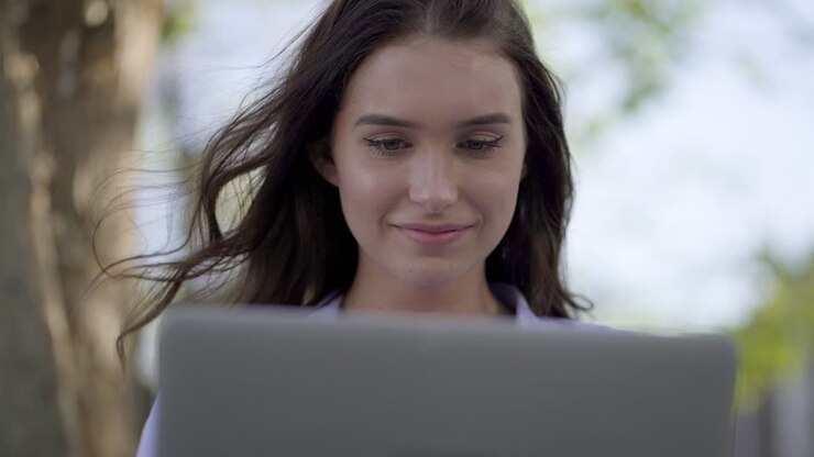 Closeup of woman in park working on laptop, correcting her hair