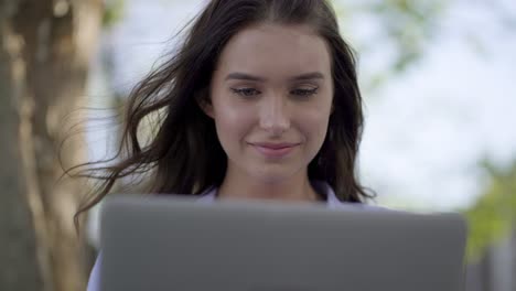 closeup of woman in park working on laptop, correcting her hair