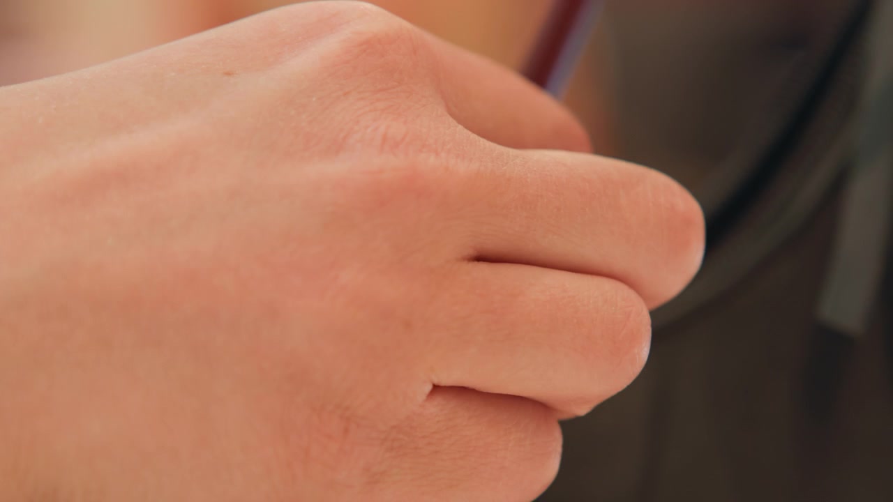 Tight low-angle close-up shows hand and fingers gently gripping curved mirror rim mounted on dark textured surface, with slight blur, warm indoor light, reflective highlights, and intimate detail