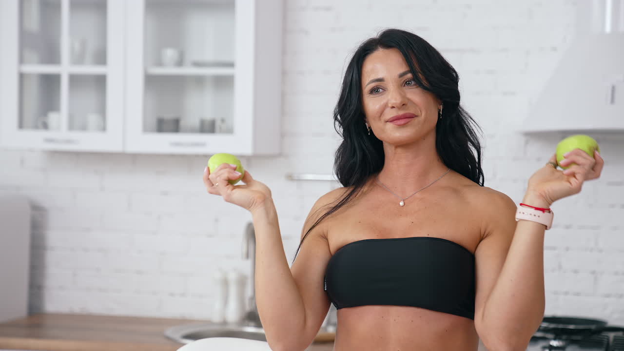 Donna felice in cucina che gioca con una mela. Una casalinga che fa una colazione sana.