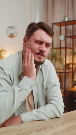 caucasian young man freelancer sitting at home office table feeling toothache touching mouth at home