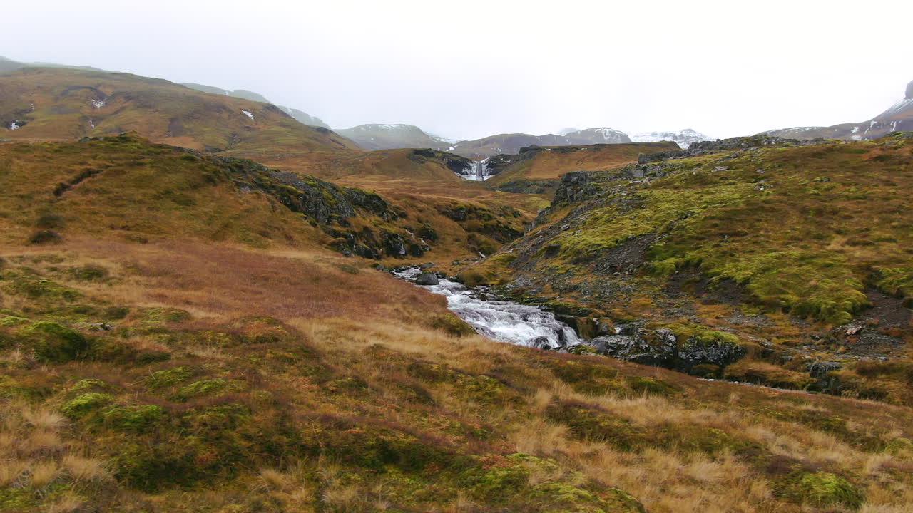 Panoramic drone view of overcast skies, multiple mountains, brush covered ground, valleys and waterfalls in Iceland Kirkjufell Mountain near Grundarfjordour