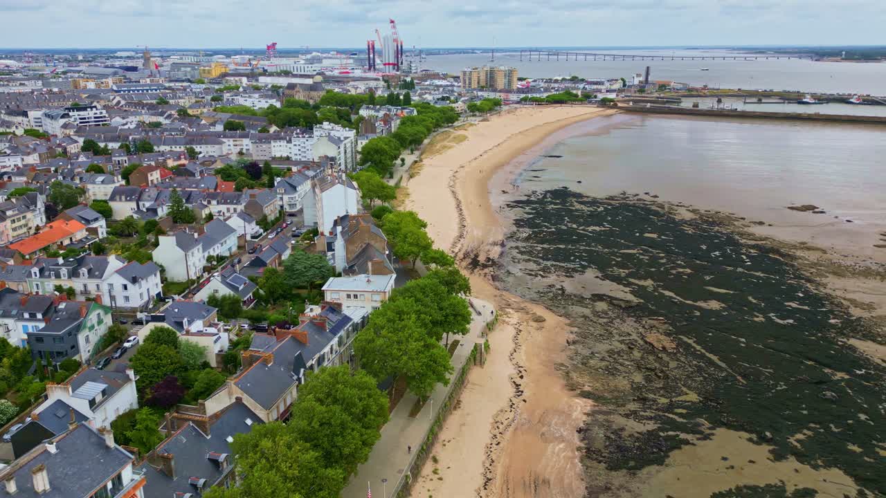 Aerial drone shot moving upward and sideways above Petit Traict beach, low tide, algae, and Saint-Nazaire houses in France
