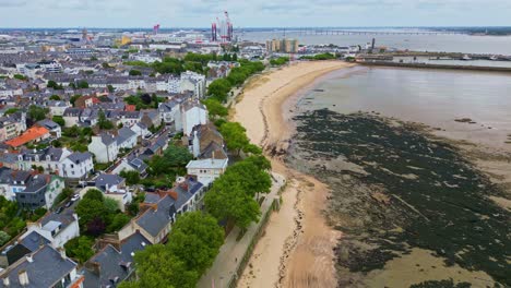 aerial drone shot moving upward and sideways above petit traict beach, low tide, algae, and saint-nazaire houses in france