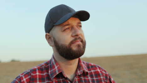 close up of the good looking farmer wearing a baseball hat looking at the horizon and thinking