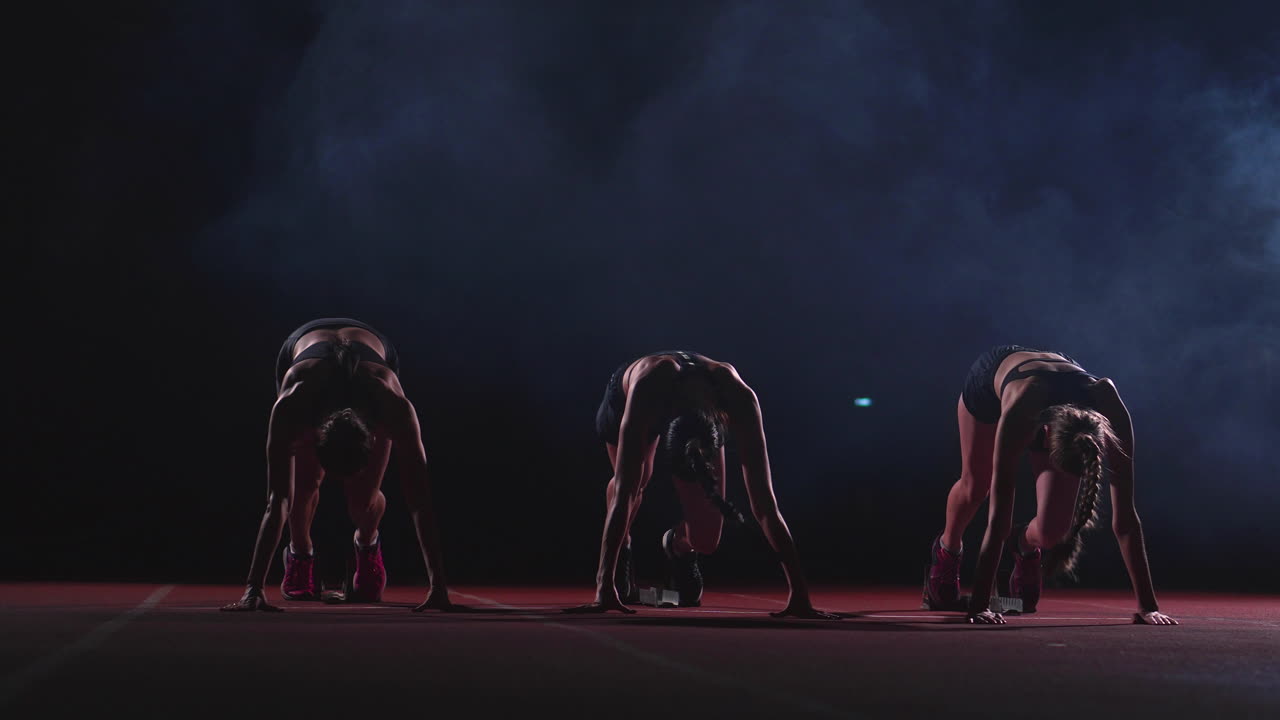 육상 트랙의 여자 달리기 선수들이 경주 전에 출발 블록에 앉아 있습니다. 슬로우 모션으로.