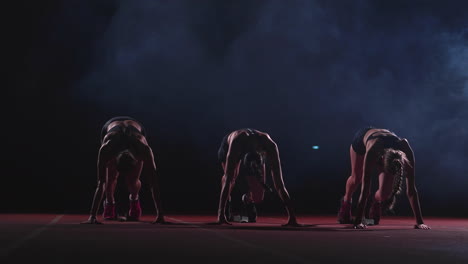 female runners at athletics track crouching at the starting blocks before a race. in slow motion.