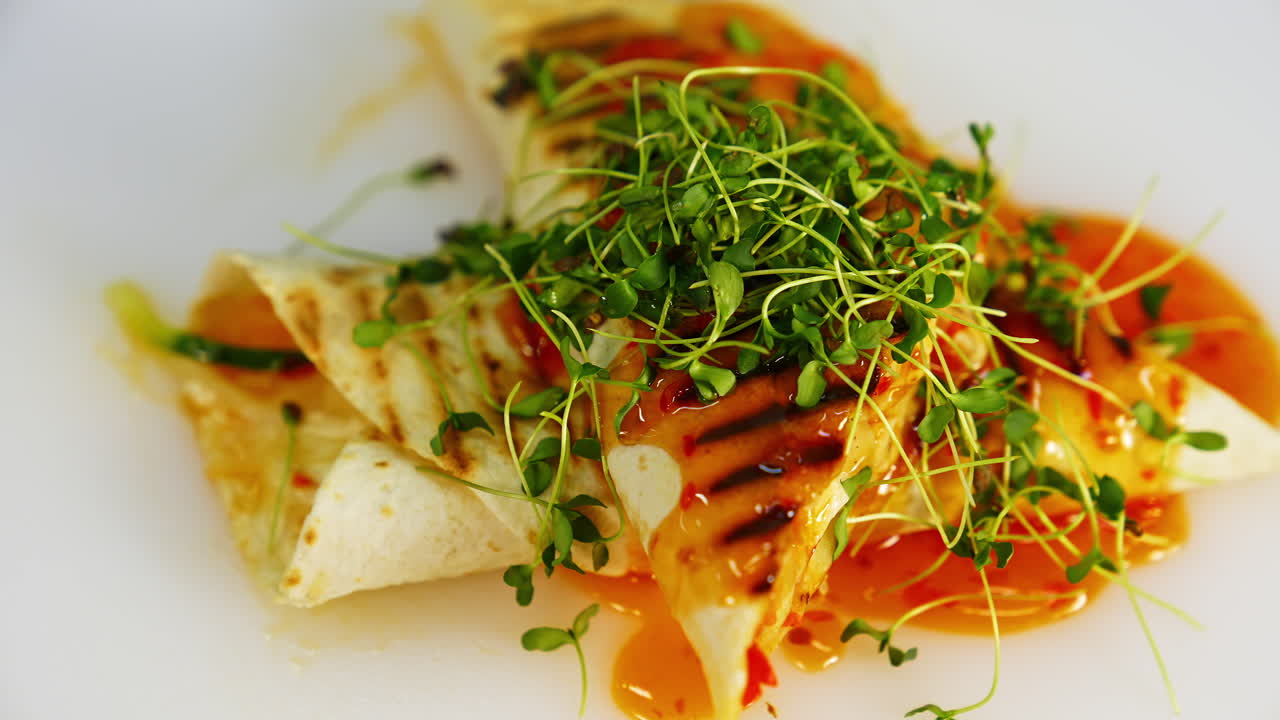 Tasty appetizer. Red sauce is pouring on a delicious cooked pita that is spinning on white plate. Tasty dish with green sprouts in a restaurant.