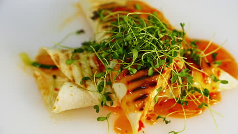 tasty appetizer. red sauce is pouring on a delicious cooked pita that is spinning on white plate. tasty dish with green sprouts in a restaurant.