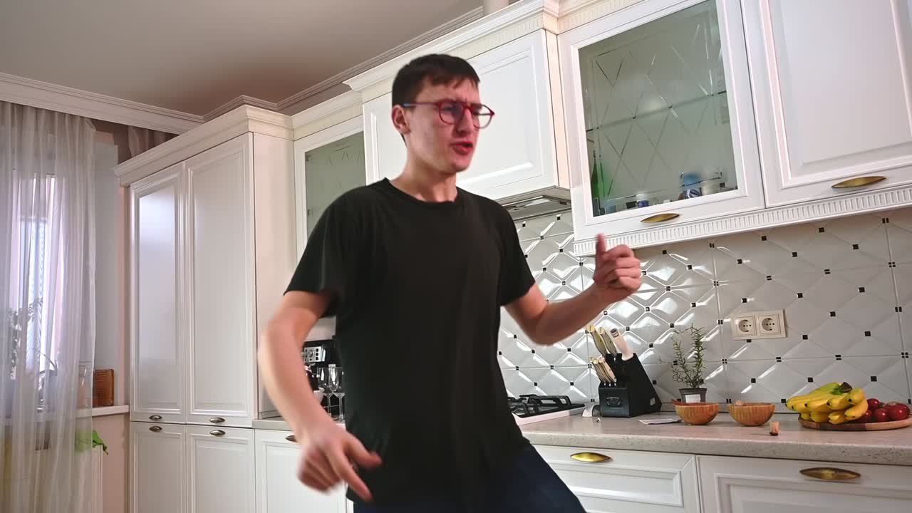 Young man dancing in a white modern kitchen with wine and fruits in background. Bottom view. Slow motion