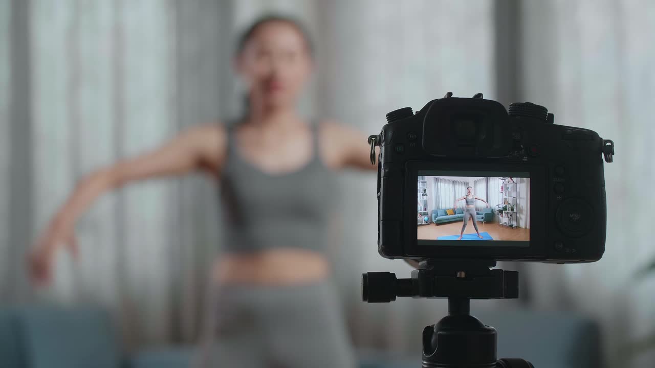 in der nähe eines kameramonitors, der eine asiatische trainerin in sportkleidung aufzeichnet, die spricht und sich streckt, während sie zu hause übungen unterrichtet