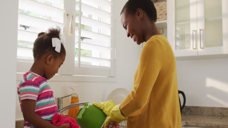 happy african american mother and daughter washing dishes in kitchen