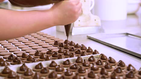 baker squeezing piping bag with ganache chocolate on macaroons