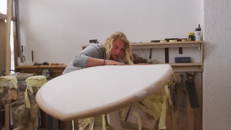 Caucasian-male-surfboard-maker-making-a-surfboard-and-preparing-to-polishing