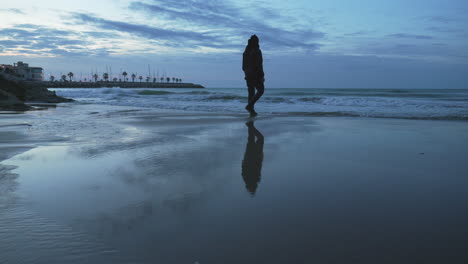 Playa-Crepuscular-Con-Silueta-De-Hombre-Saltando-Sobre-Charco,-Reflejo-De-Marea-Baja