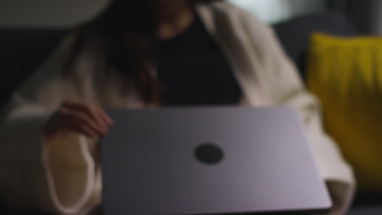 소파에 앉아서 인터넷을 탐색하기 위해 노트북을 열고 집에서 저녁을 보내는 여성의 클로즈업