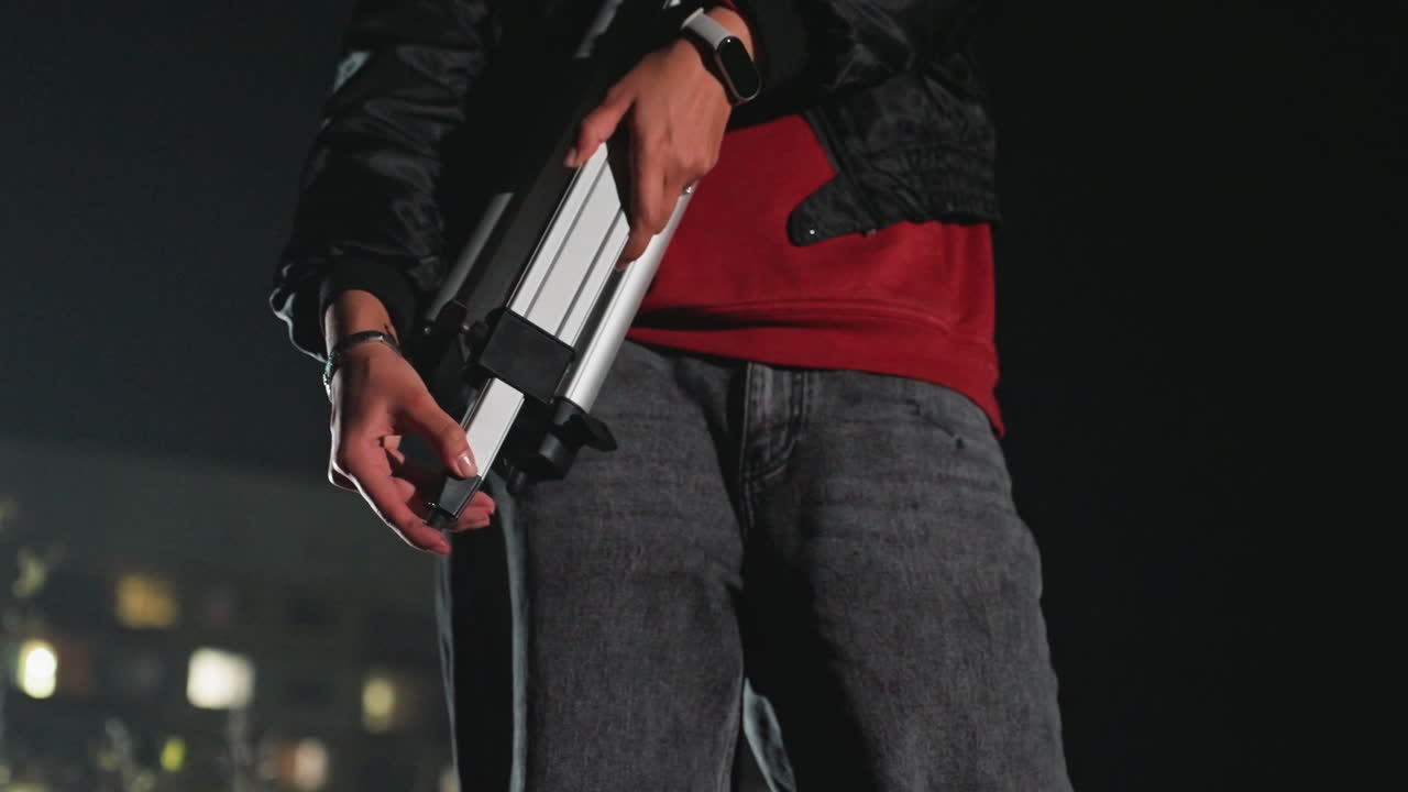 asian male on rooftop adjusting telescope, aims instrument toward star field, urban skyline bokeh, tripod handling, red sweater under leather jacket, careful calibration, cinematic lowlight
