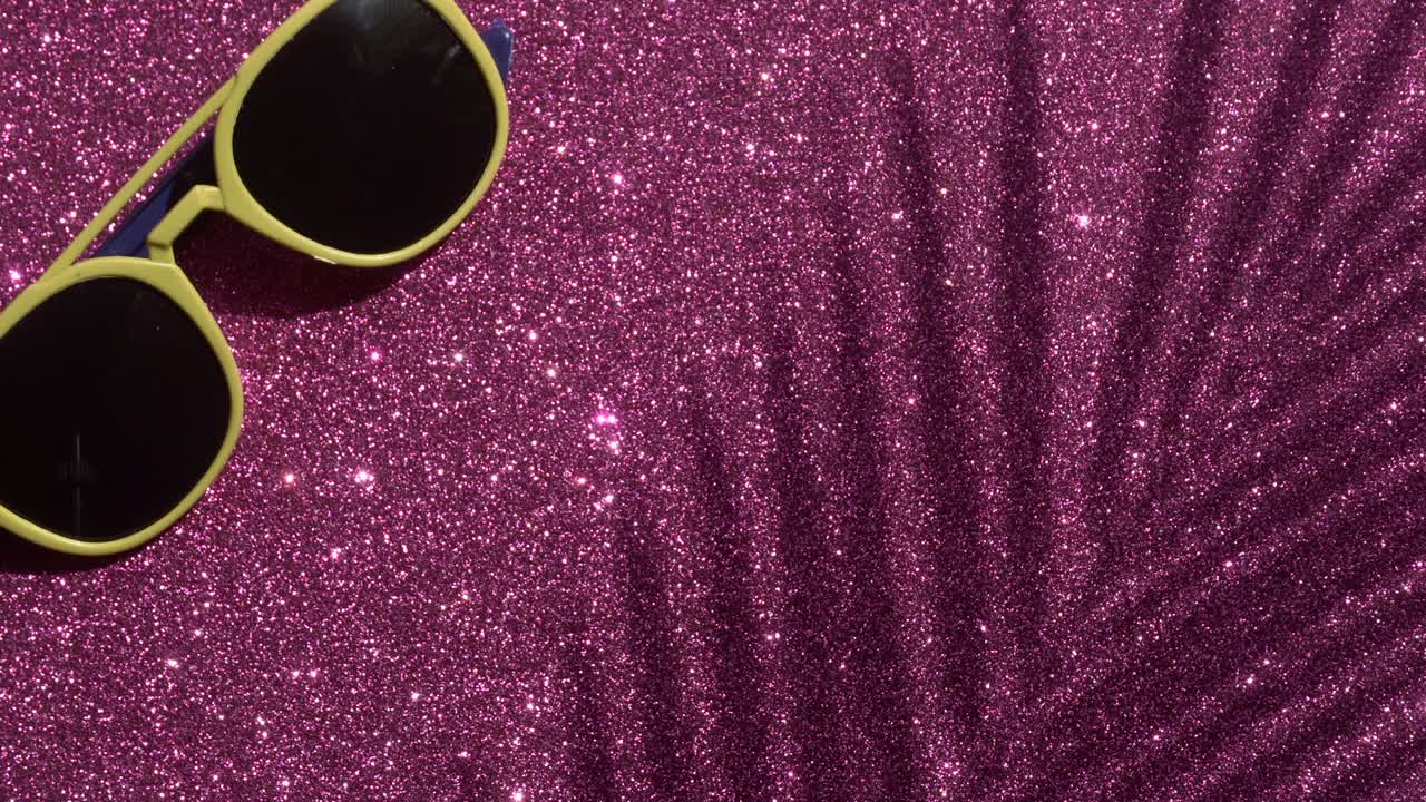 Shadows from a palm tree with sunglasses on a pink glitter sparkling shining background. Minimal art, glamor, vacation, summer, party concept.