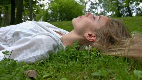 a pretty woman lies on grass in the green city park in summer and smiling to camera