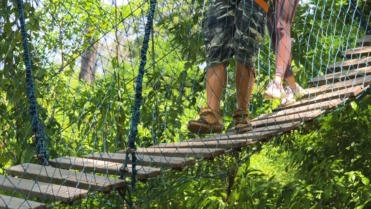 Couple Walking Across a Wooden Suspension Bridge in a Treetop Adventure Park