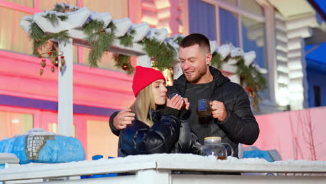happy caucasian man stands embracing his wife. beautiful couple enjoys hot tea outdoors in winter near beautiful cottage.