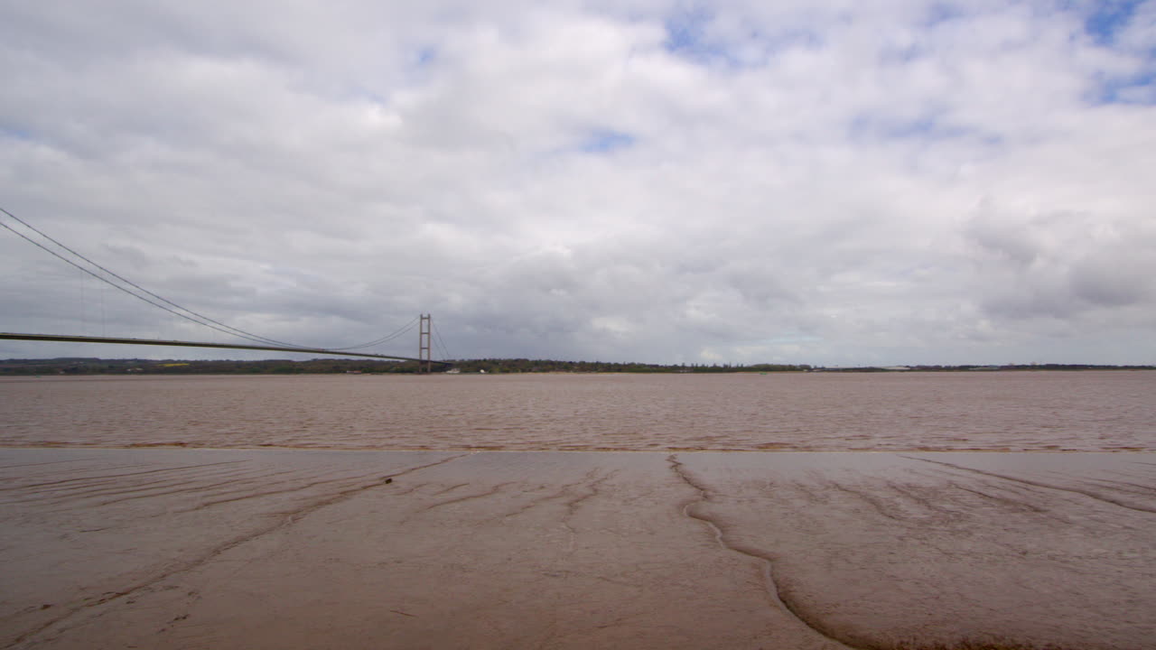 panning wide shot of the Humber bridge showing exposed mud flats on the Humber estuary with footpath